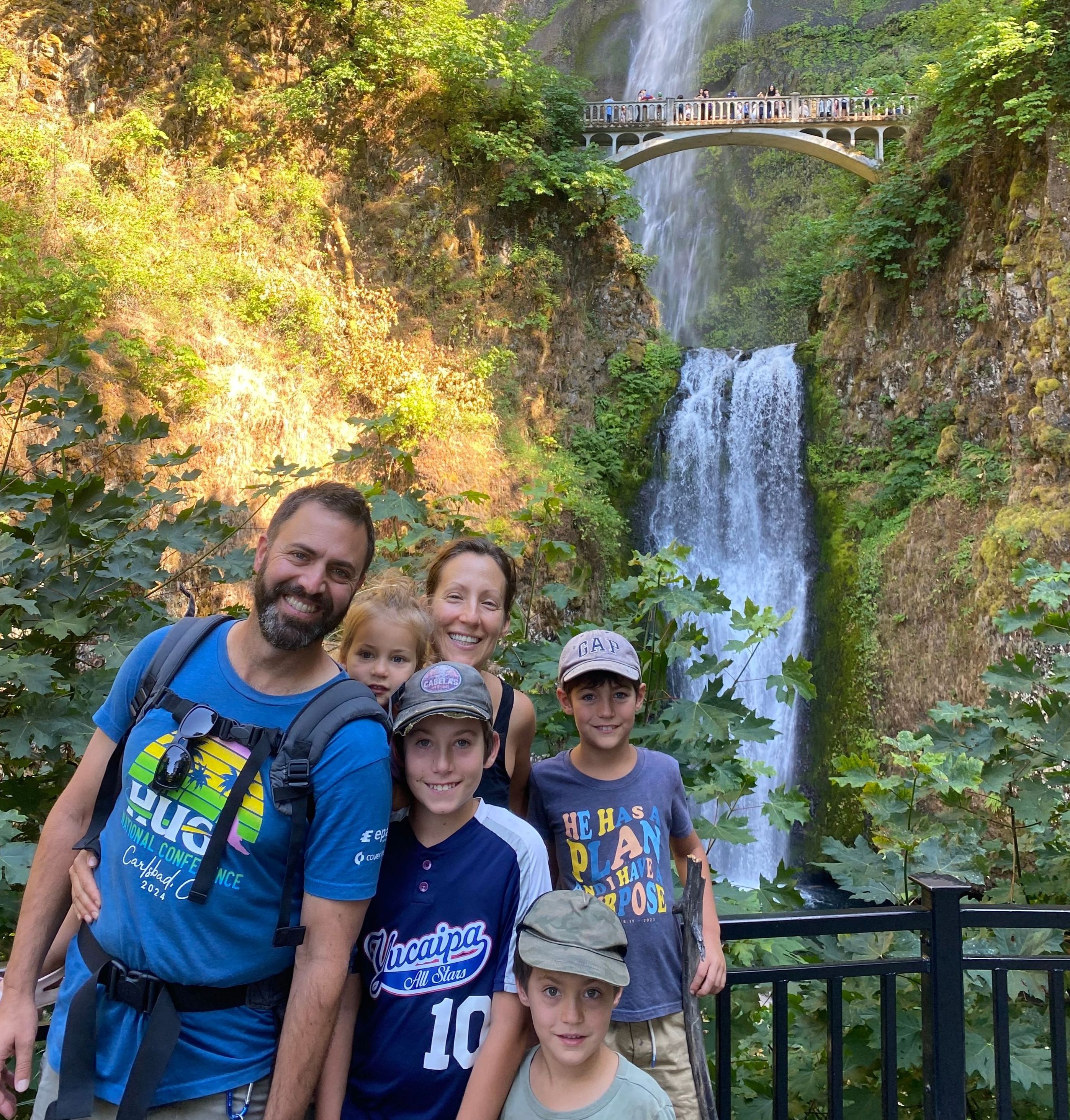 Eli and his family on vacation posing in front of a bridge over a waterfall in Multnomah Falls, Oregon.